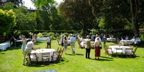 Alumni and guests in the President's Garden with tables set up with white tablecloths and wooden chairs.