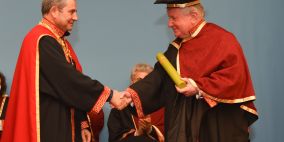 Two men in red robes shaking hands at a graduation ceremony