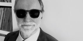 A black and white photo of Sir Robin Millar, Honorary Fellow. Robin is dressed in a suit and wearing dark glasses.