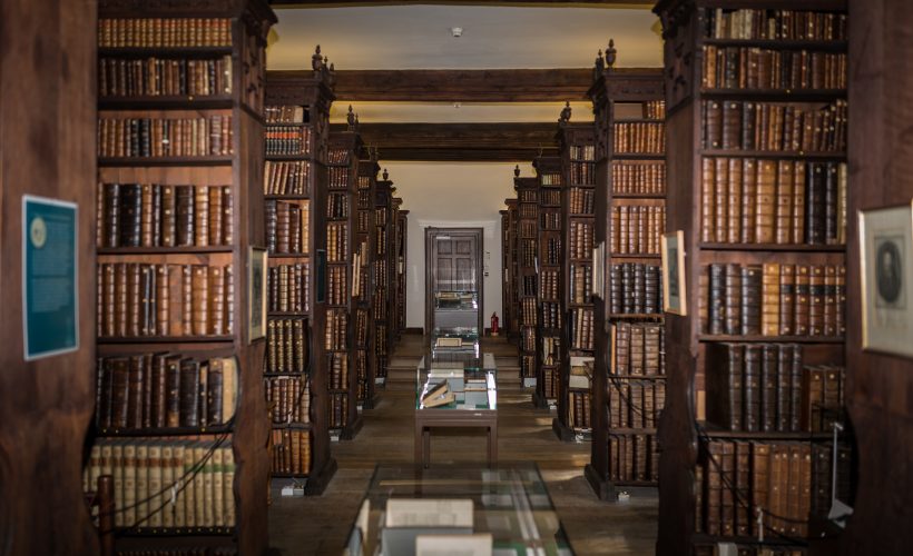 Interior of a historic library with tall wooden shelves packed with old books, glass display tables along the aisle.
